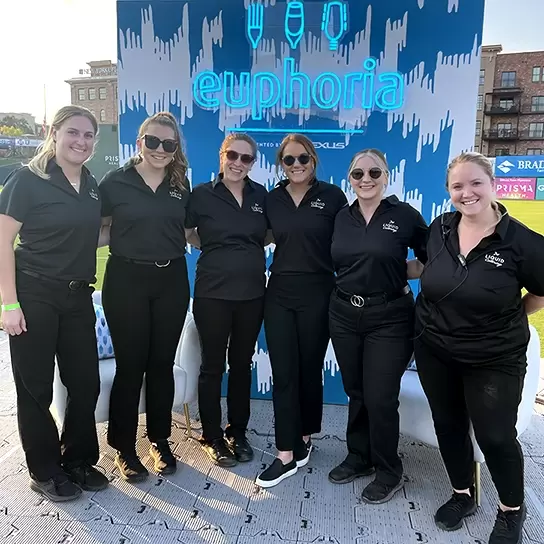 Six bartenders post together in front of the Euphoria sign in their black Liquid Catering uniforms.